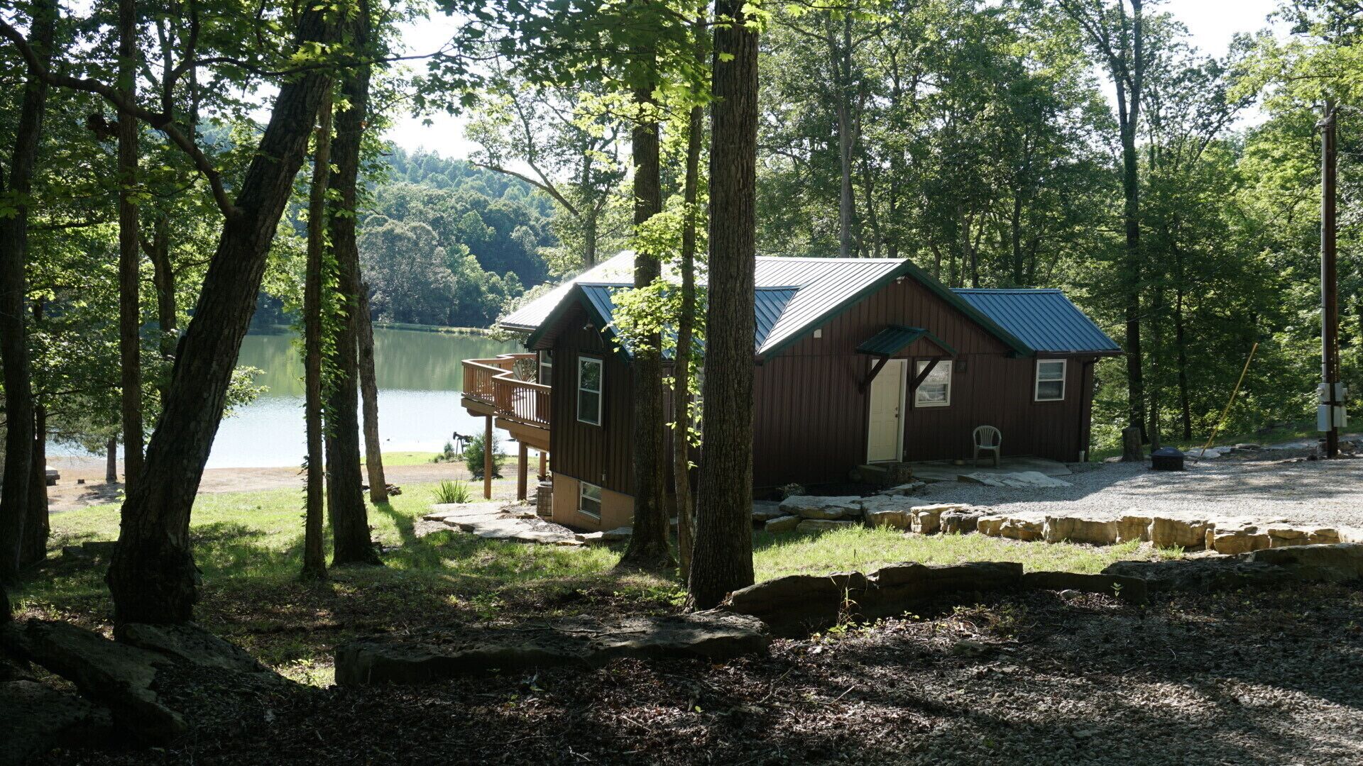 A cabin with a deck, surrounded by trees and a lake.