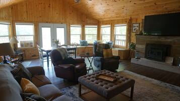 A cozy cabin interior with a fireplace, wooden walls, and large windows.
