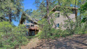A two-story cabin with a balcony, surrounded by dense forest.