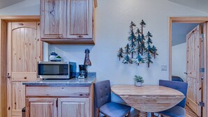 A compact kitchen with wooden cabinets, a microwave, a coffee maker, and a dining area with a round table and blue chairs.