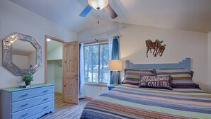 A bedroom with a bed, a dresser, a mirror, a window with curtains, a ceiling fan, and a wall decoration.