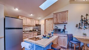 A modern kitchen with wooden cabinets, a stainless steel refrigerator, a built-in island with stools, and a dining area with a wooden table and chairs.