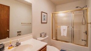 Et badeværelse med et stort spejl, en vask, et toilet og en brusekabine med glasvægge.