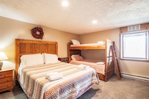 A bedroom with a wooden headboard, a bunk bed, a ladder, a bedside table with a lamp, and a window with a view. - Timberly - Hot Tub, Dog Friendly, Lake Privileges (Davis)