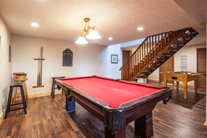 A pool table with a red felt surface, a wooden staircase, and a wooden floor.