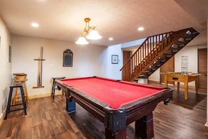 A pool table with a red felt surface, a billiards cue, and a foosball table in a room with wooden flooring and a staircase. - Timberly - 699 Ridge Road

Timberly - Private Wooded Lot, Outdoor Hot Tub, Pool Table, Pet Friendly, Lake Access! (Davis)