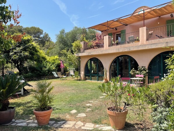 A two-story building with a covered patio, outdoor seating, and a garden area with potted plants.
