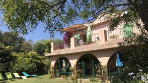 Un edificio de dos pisos con balcón, ventanas en arco y un jardín con sillas de jardín.