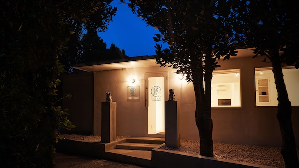 A modern building with a well-lit entrance, a visible door, and a small outdoor area with steps leading to the entrance. - Adan Resort EN (Motobu)