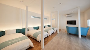A hotel room with four beds arranged in a row, a blue bathtub, and a flat-screen TV mounted on the wall. - Adan Resort EN (Motobu)