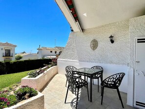 Um pátio externo com mesa e cadeiras, uma parede branca com textura e vista para edifícios vizinhos.