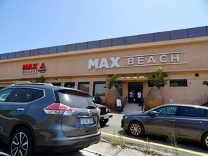 Um edifício com uma placa indicando 'MAX BEACH' e um estacionamento com carros.