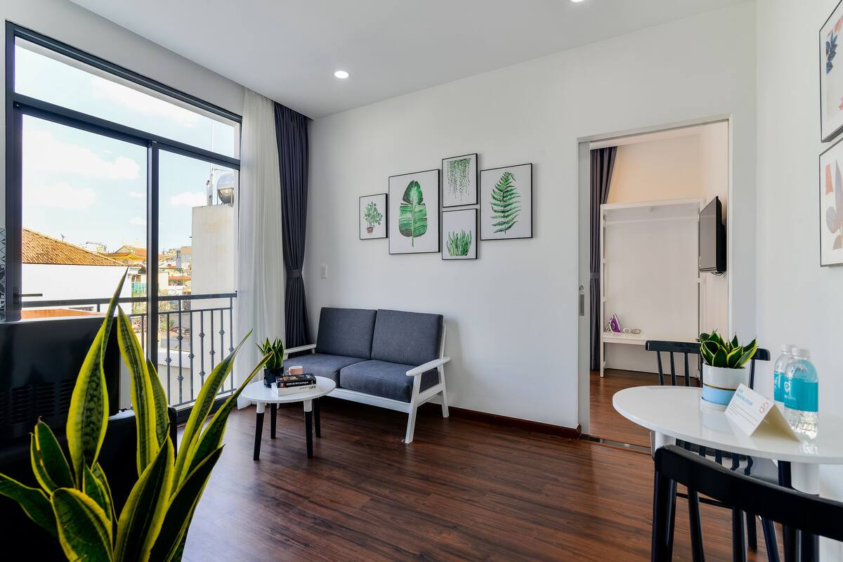 Ein modernes Wohnzimmer mit einer Couch, einem Couchtisch und einem Essbereich mit Tisch und Stühlen. Übertöpfe und gerahmte Pflanzenbilder zieren die Wand.