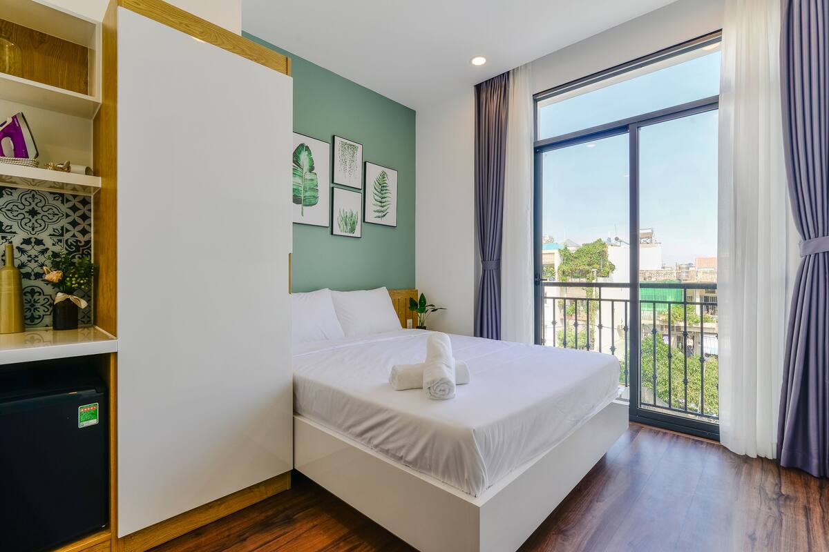 Ein modernes Hotelzimmer mit einem großen Bett, einer eingebauten Garderobe, einem kleinen Schreibtisch und einem Balkon mit Blick auf die Stadt.