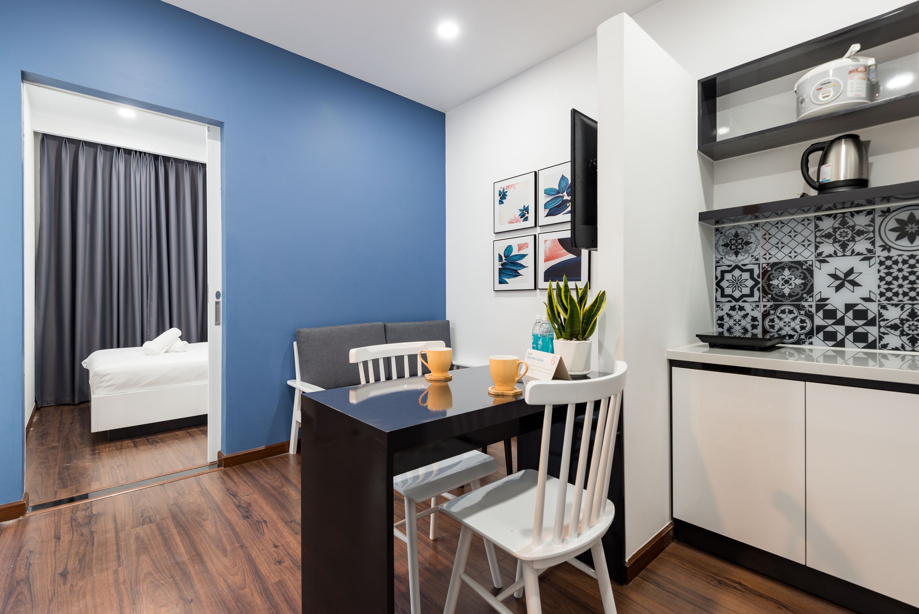 Una habitación compacta con una cama, una mesa de comedor con sillas, una zona de cocina con microondas y un televisor en la pared.