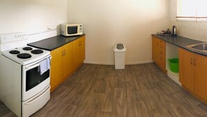 A compact kitchen with a white stove, microwave, and wooden cabinets. - House with self-contained adjoining studio. Great for large groups (Auckland)