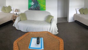 A hotel room with a white sofa, a small side table with a lamp, a remote control on a woven tray, and a painting on the wall. - House with self-contained adjoining studio. Great for large groups (Auckland)