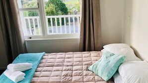 A bedroom with a bed, a window with curtains, and a view of greenery outside. - House with self-contained adjoining studio. Great for large groups (Auckland)
