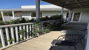 A covered porch with a wooden deck, white railings, and two metal chairs. - House with self-contained adjoining studio. Great for large groups (Auckland)