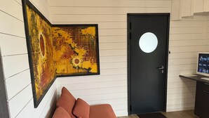 Una habitación con una puerta negra, un cuadro abstracto enmarcado, un sofá marrón con cojines y un escritorio pequeño con un monitor de computadora.