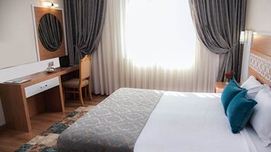 A hotel room with a bed, a desk, a chair, a mirror, and a window with curtains. - Met Gold Hotel (Gaziantep)