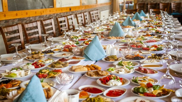 A long dining table with various dishes and glasses, set in a room with wooden chairs and a stone wall. - Met Gold Hotel (Gaziantep)