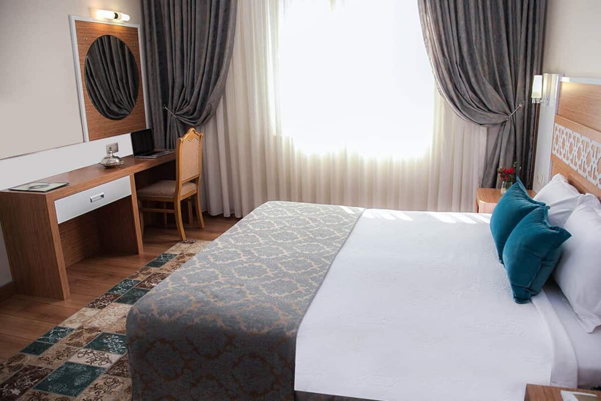 A hotel room with a bed, a desk, a chair, a mirror, and a window with curtains.