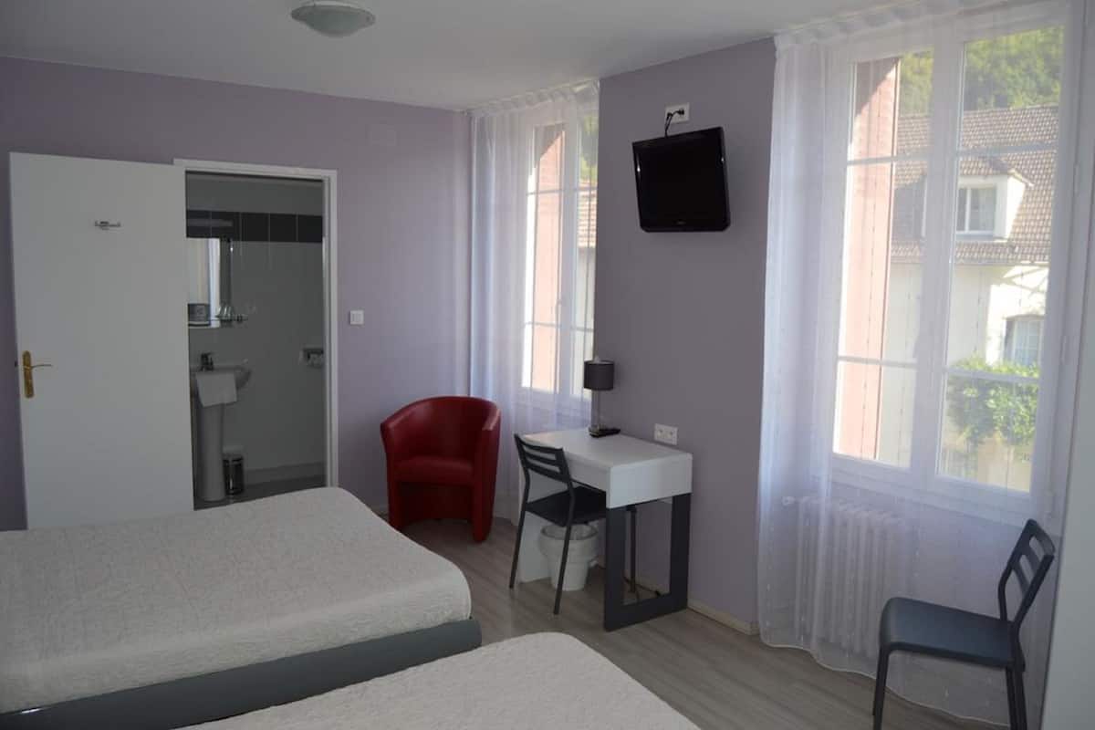 Una habitación con dos camas, un escritorio con silla, un televisor y una ventana con cortinas.