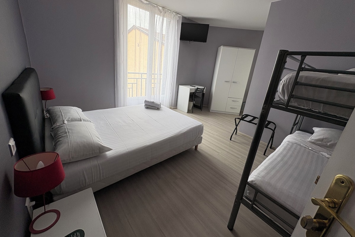 Habitación de hotel con una cama individual, un escritorio con silla, una cama nido, un armario y un televisor en la pared.