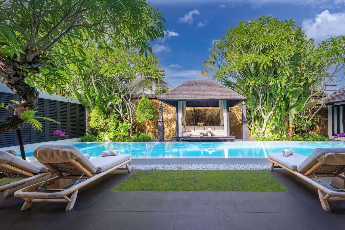 A pool area with lounge chairs, a gazebo, and lush greenery.