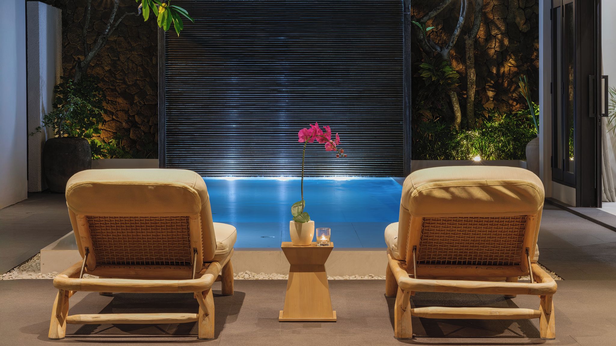 Two wicker chairs facing a blue pool with a pink flower centerpiece.