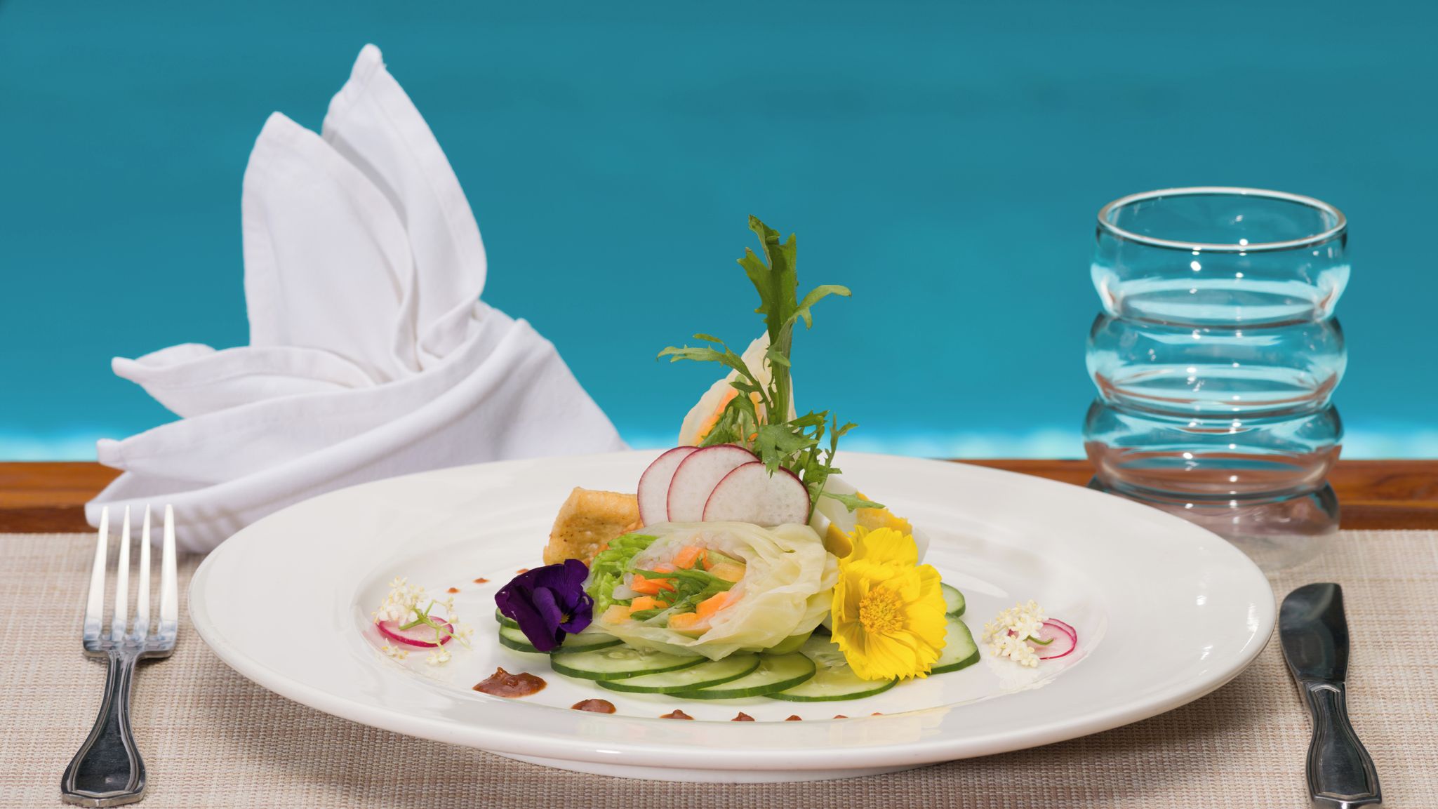 A plate of food with a folded napkin and a glass of water on a table.