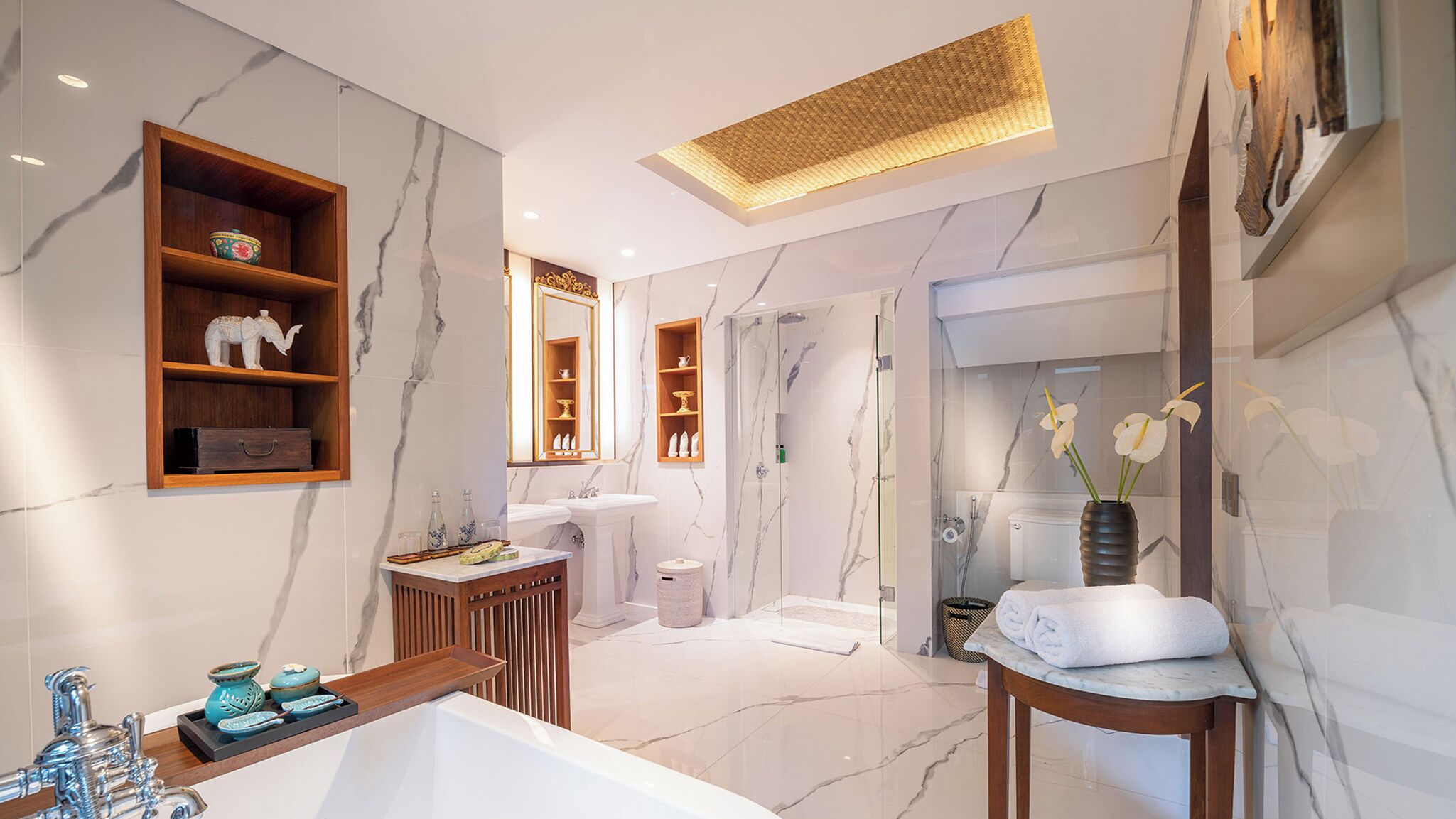 A modern bathroom with marble walls, a large bathtub, a glass-enclosed shower, and a vanity with a mirror.