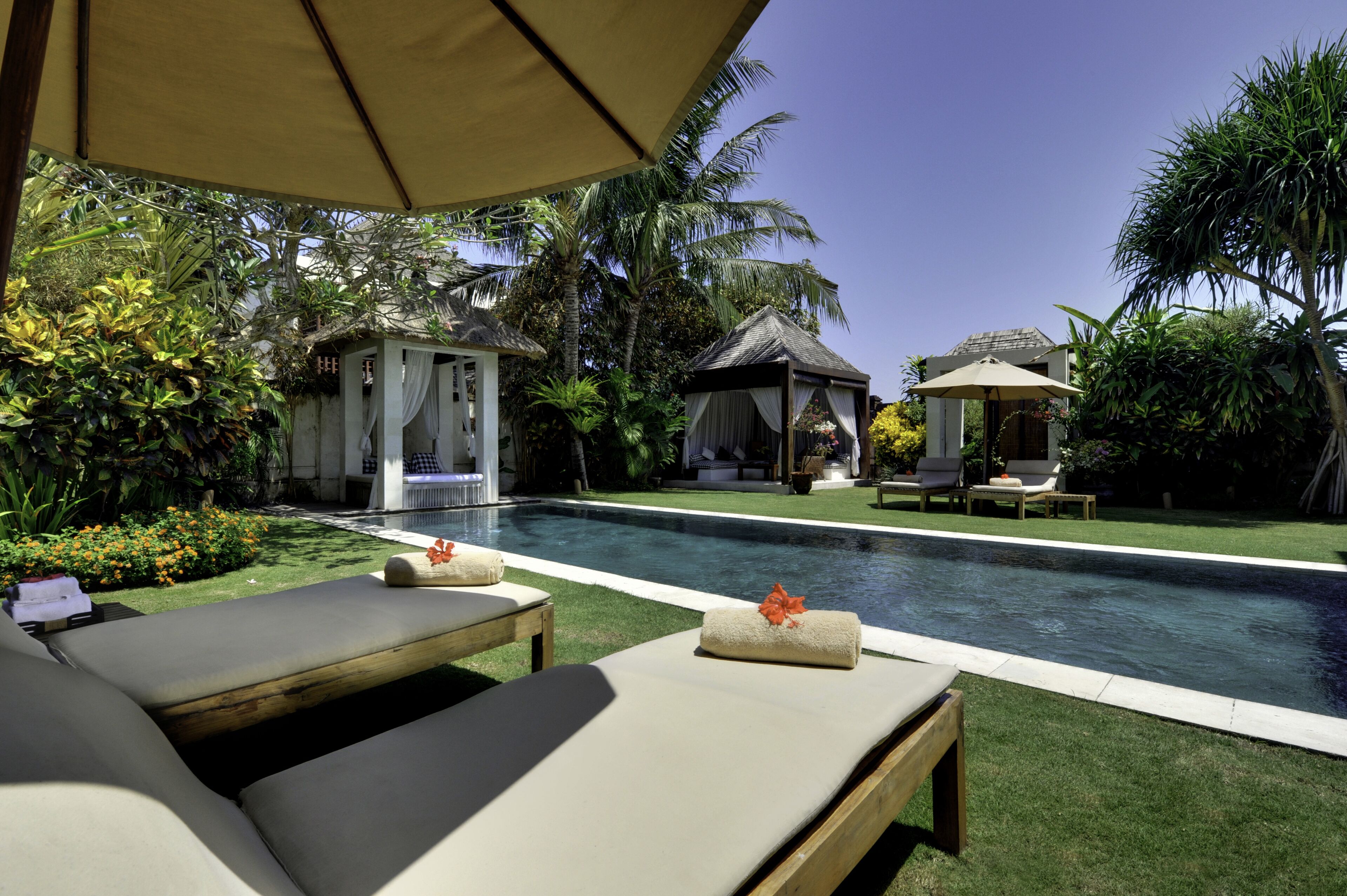 A poolside area with lounge chairs, a small gazebo, and a thatched-roof structure.