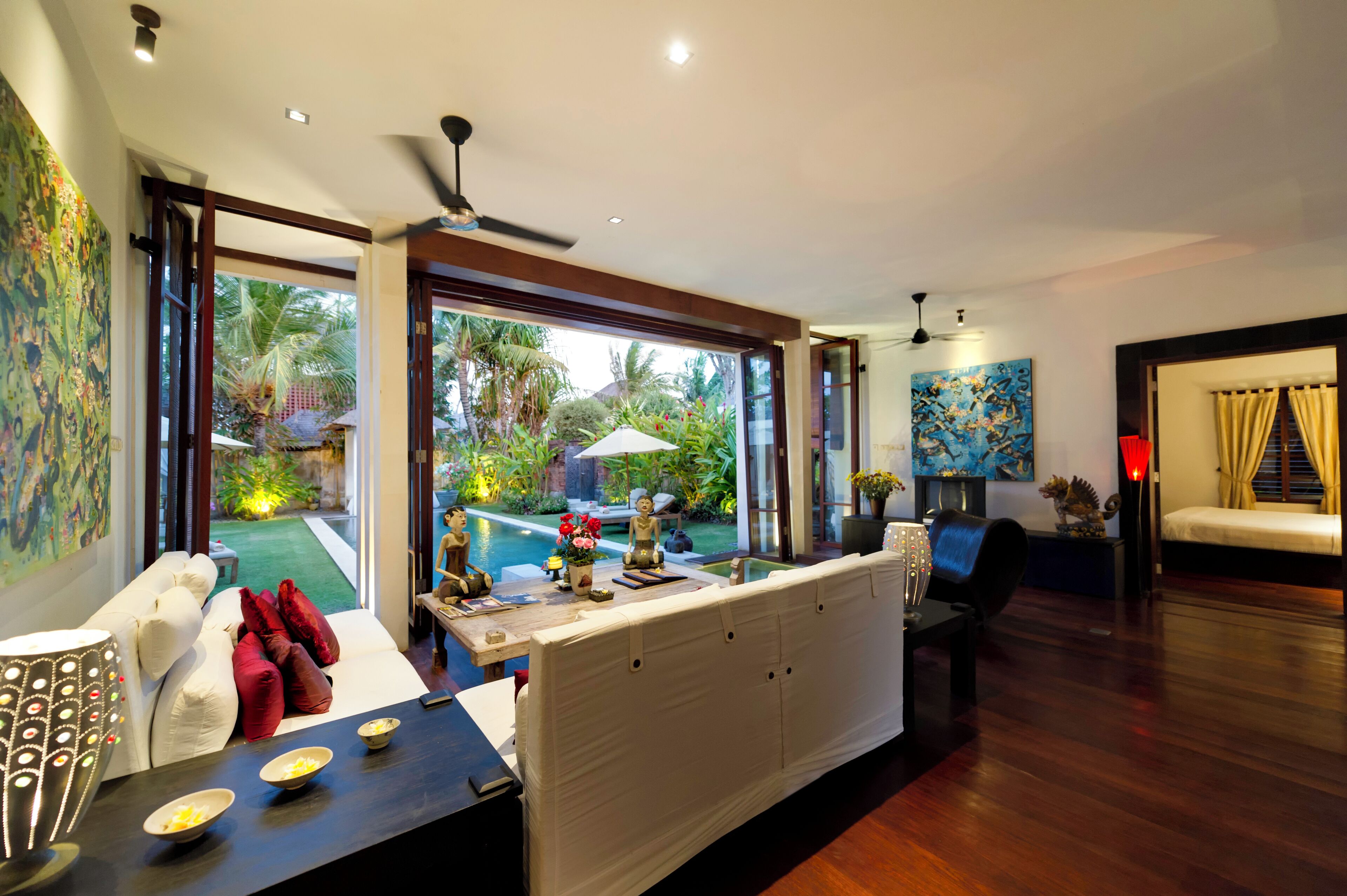A modern living room with a large window, a sofa, a dining table, and a ceiling fan.