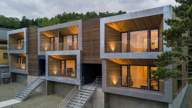 Un moderno edificio a più piani con balconi, posti a sedere all'aperto e una scala che conduce all'ingresso.