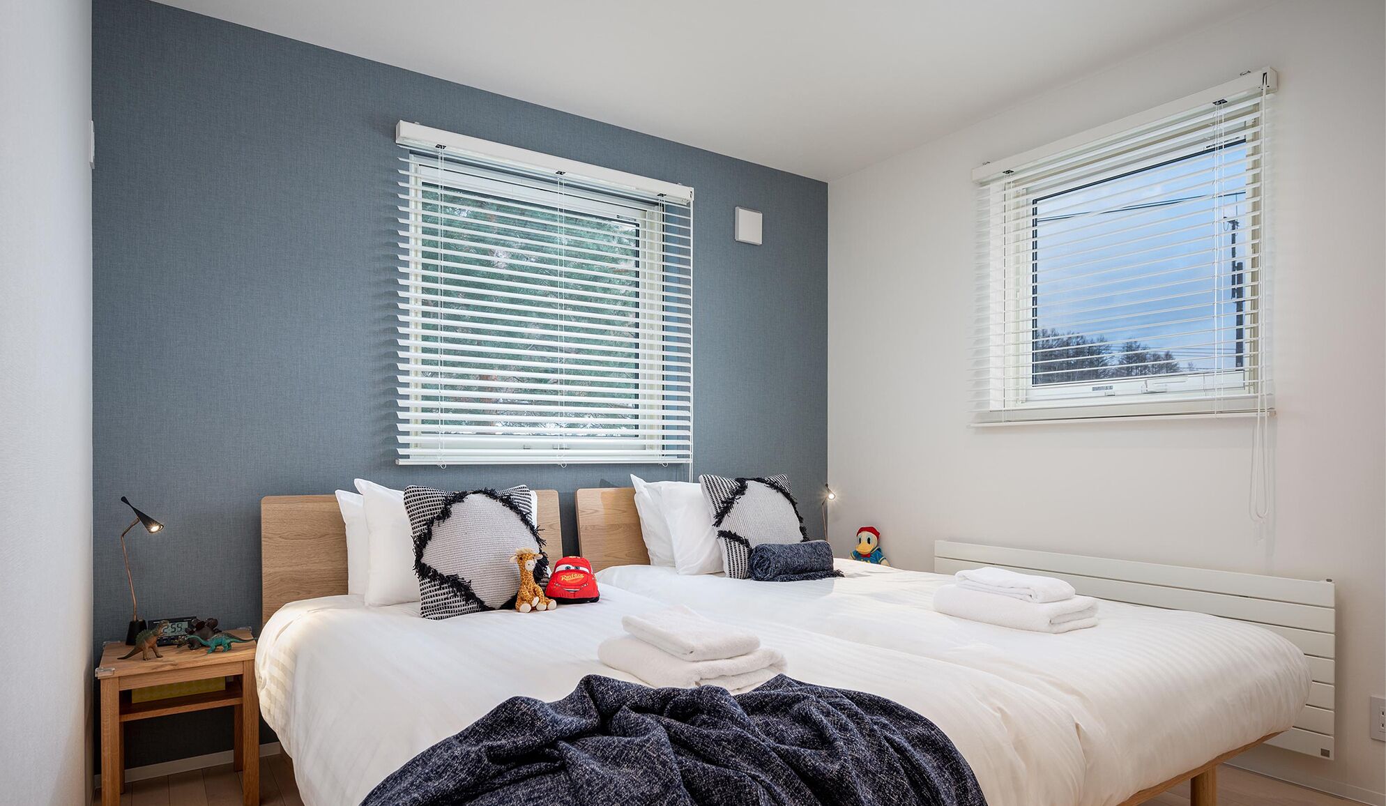 Une chambre avec deux lits, du linge de lit blanc et un mur gris.