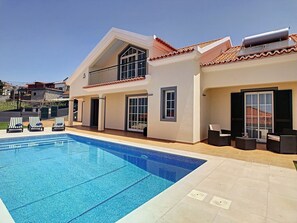 Una casa de dos pisos con piscina, mobiliario exterior y vistas del barrio.