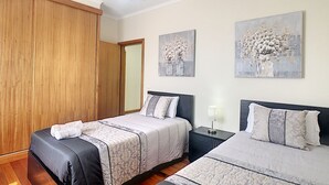 A bedroom with two beds, wooden wardrobe, and artwork on the wall.