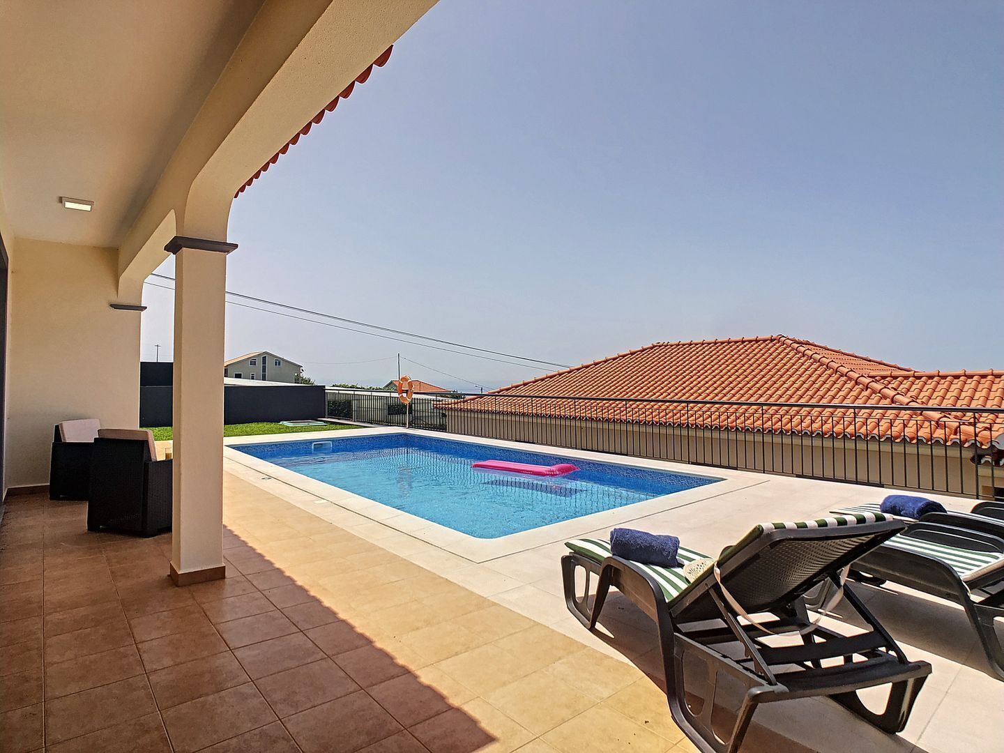 A rooftop pool area with a clear blue pool, lounge chairs, and a view of a residential neighborhood.