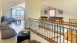 A spacious loft apartment with a high ceiling, a balcony with a view, a pool table, and a cozy seating area.