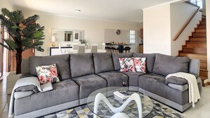 A modern living room with a grey sectional sofa, a glass coffee table, and a large potted plant.