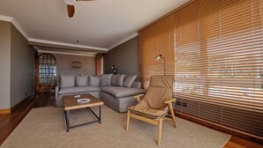 A living room with a sectional sofa, a wooden coffee table, a chair, and a large window with blinds. - Casa Ulli by LovelyStay (Canico)