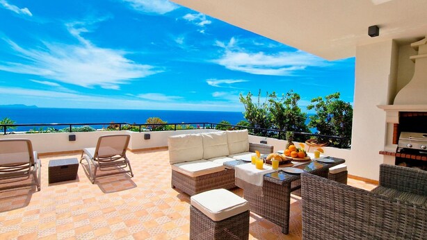 A terrace with wicker furniture, a white sofa, and a table set with fruits and drinks. - Casa Ulli by LovelyStay (Canico)