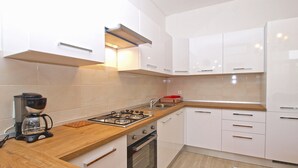 A modern kitchen with white cabinets, a gas stove, a coffee maker, and a wooden countertop. - Apartment 1347/12668 (Istria - Pula), 1500m from the beach (Pula)