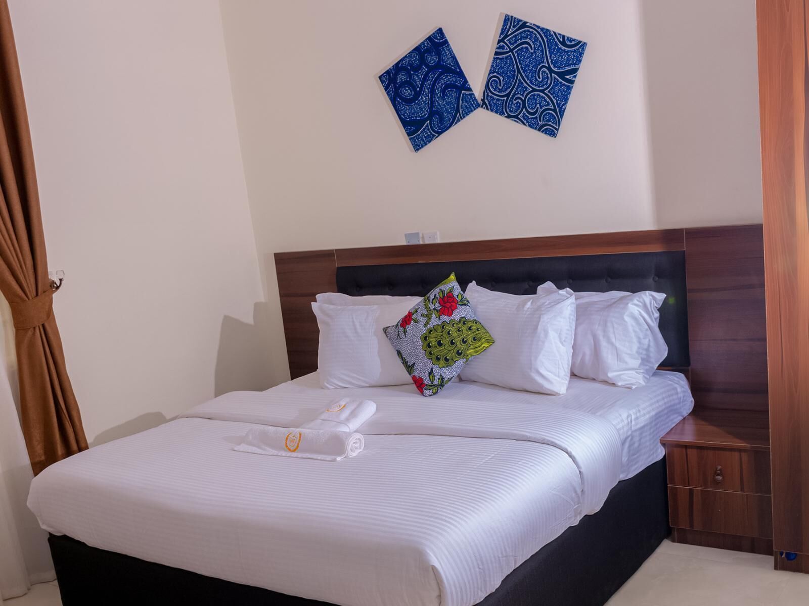 Una cama bien hecha con sábanas blancas, cabecera de madera y un cojín decorativo con estampado floral.