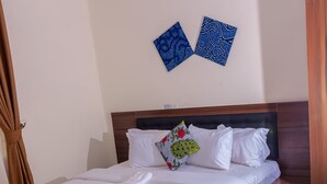 A neatly made bed with white linens and a folded towel, a wooden headboard, and a small bedside table with a drawer.