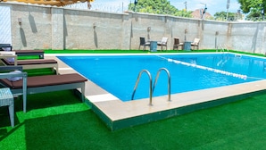 A swimming pool with a diving board, lounge chairs, and a covered seating area.