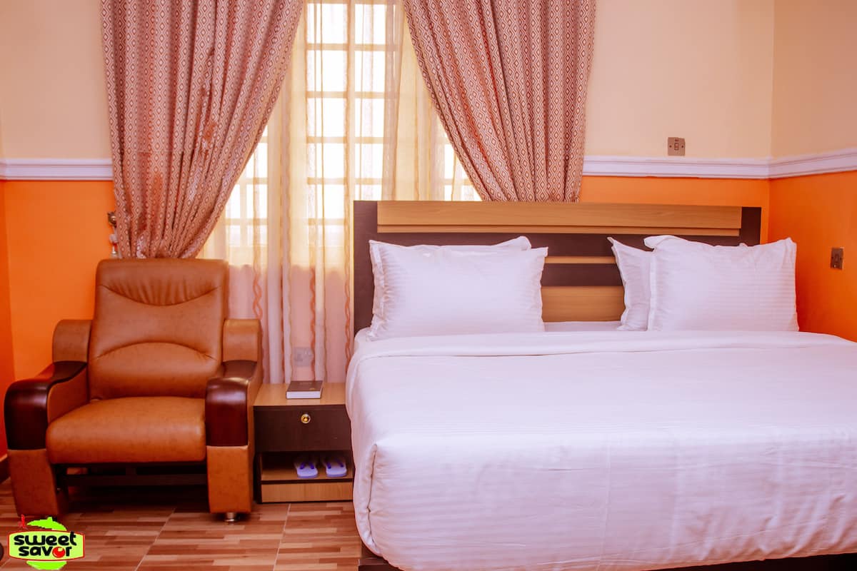 Une chambre d’hôtel avec un lit, une chaise, une table de chevet et une fenêtre avec des rideaux.