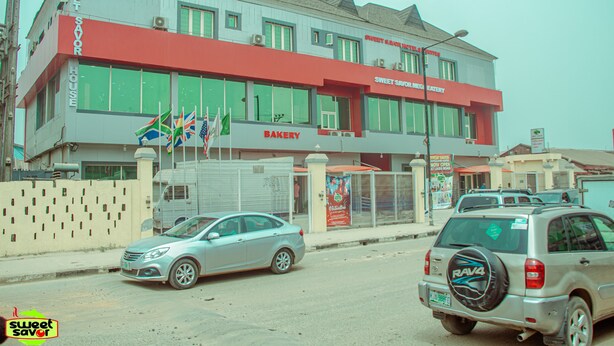 A building with a bakery sign, a flag, and parked cars. - Sweet Savor Hotels and Suites Annex (Lagos)